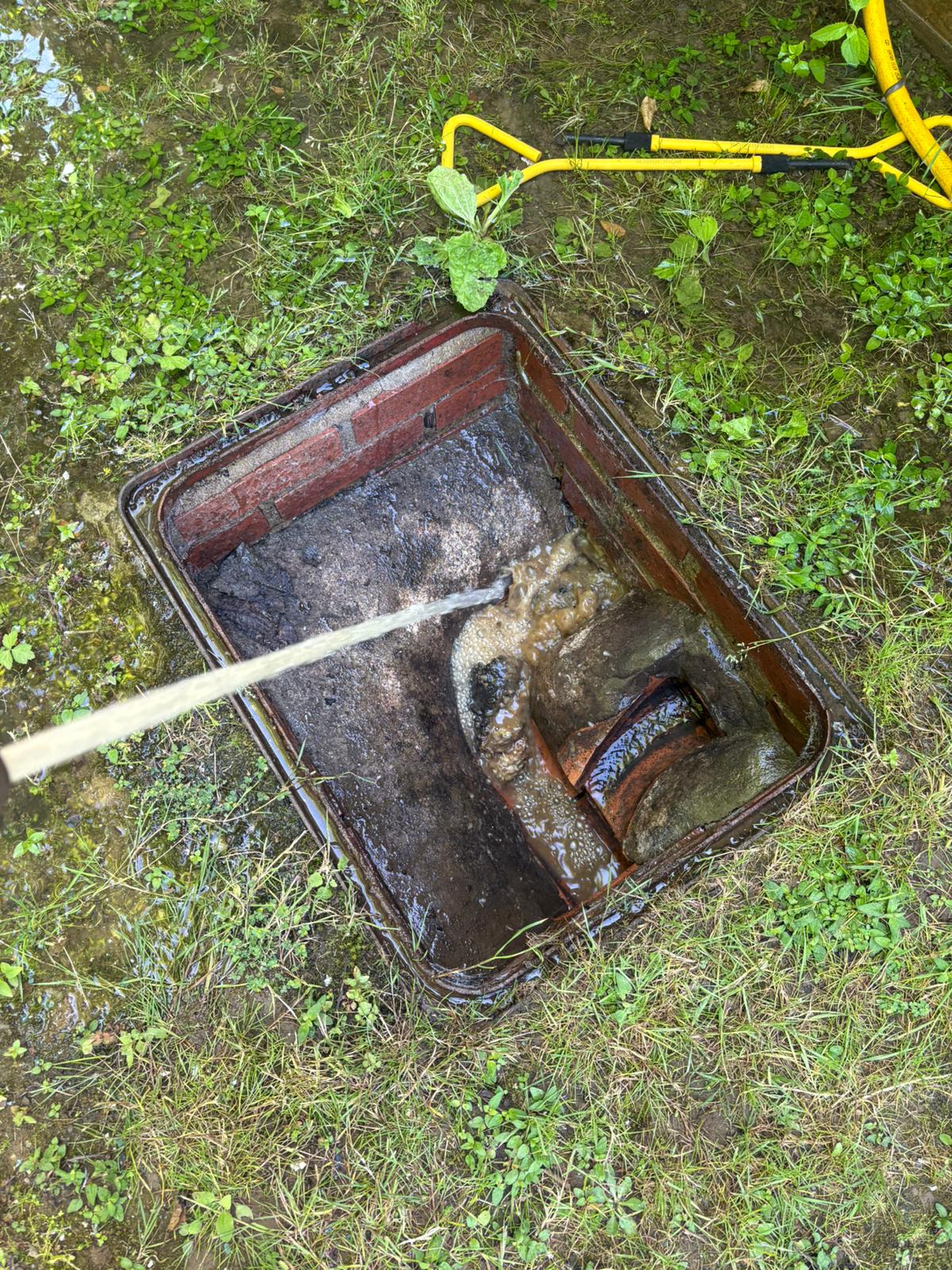 Engineer using a jetting rod in an open drain chamber to clear a blockage in Staplehurst