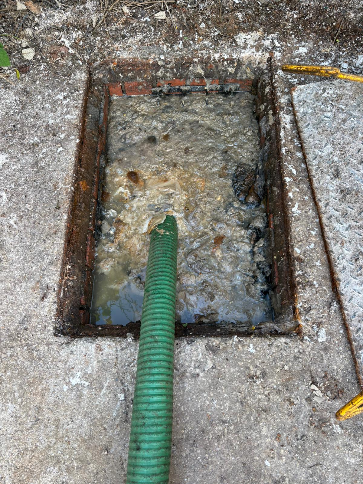 Vacuum hose clearing a blockage at an open manhole