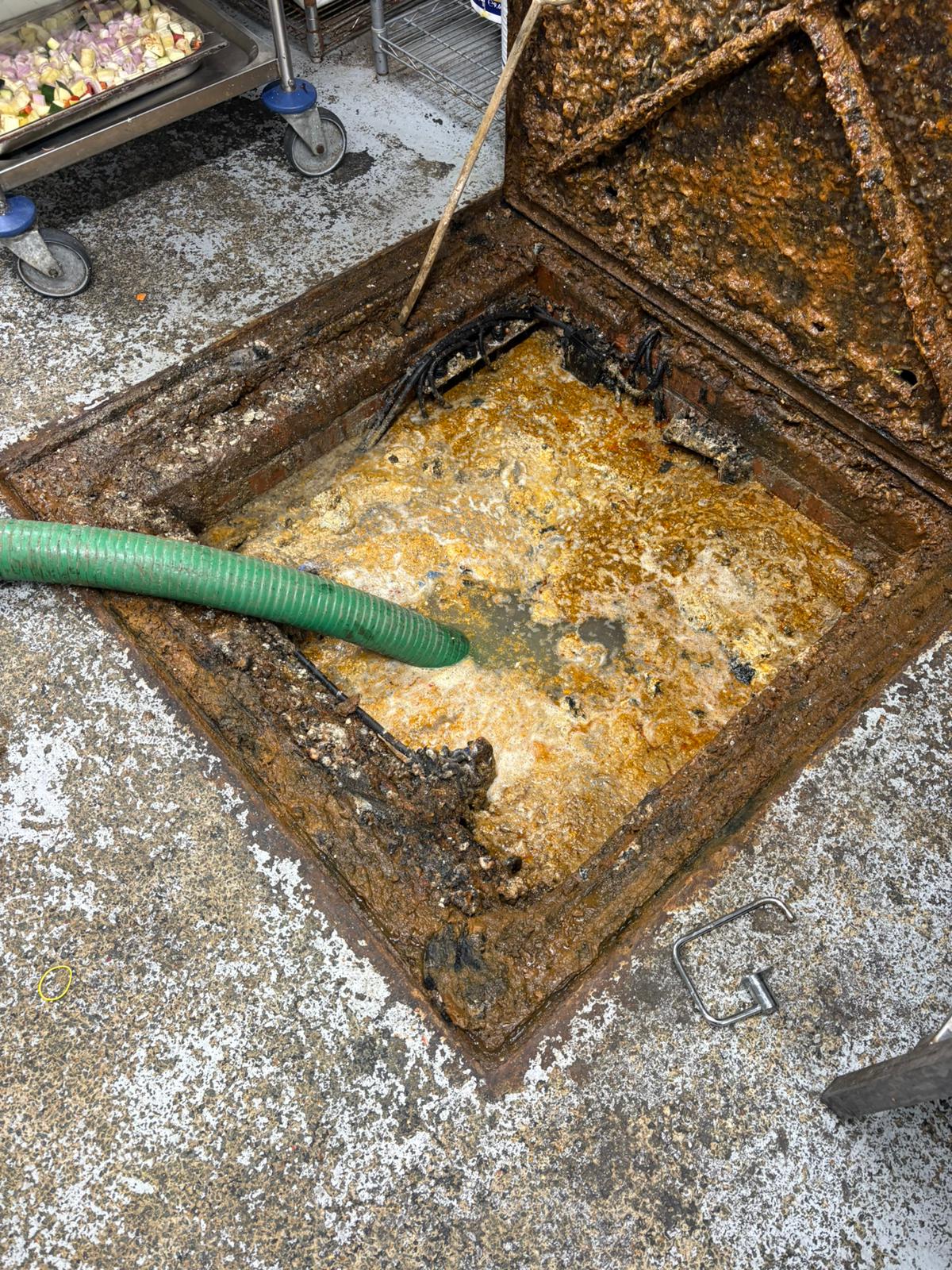 Grease trap being cleaned with a vacuum hose in a commercial kitchen in Kent, Surrey, Sussex, Essex & London